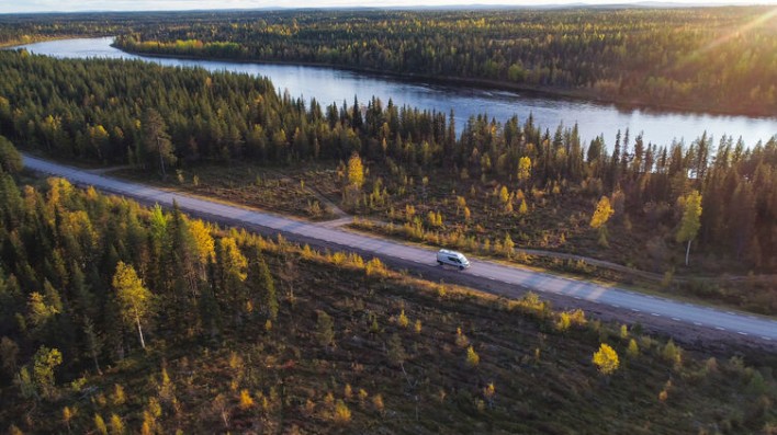 Camper fährt auf einer Landstraße durch die herbstlichen Wälder Lapplands