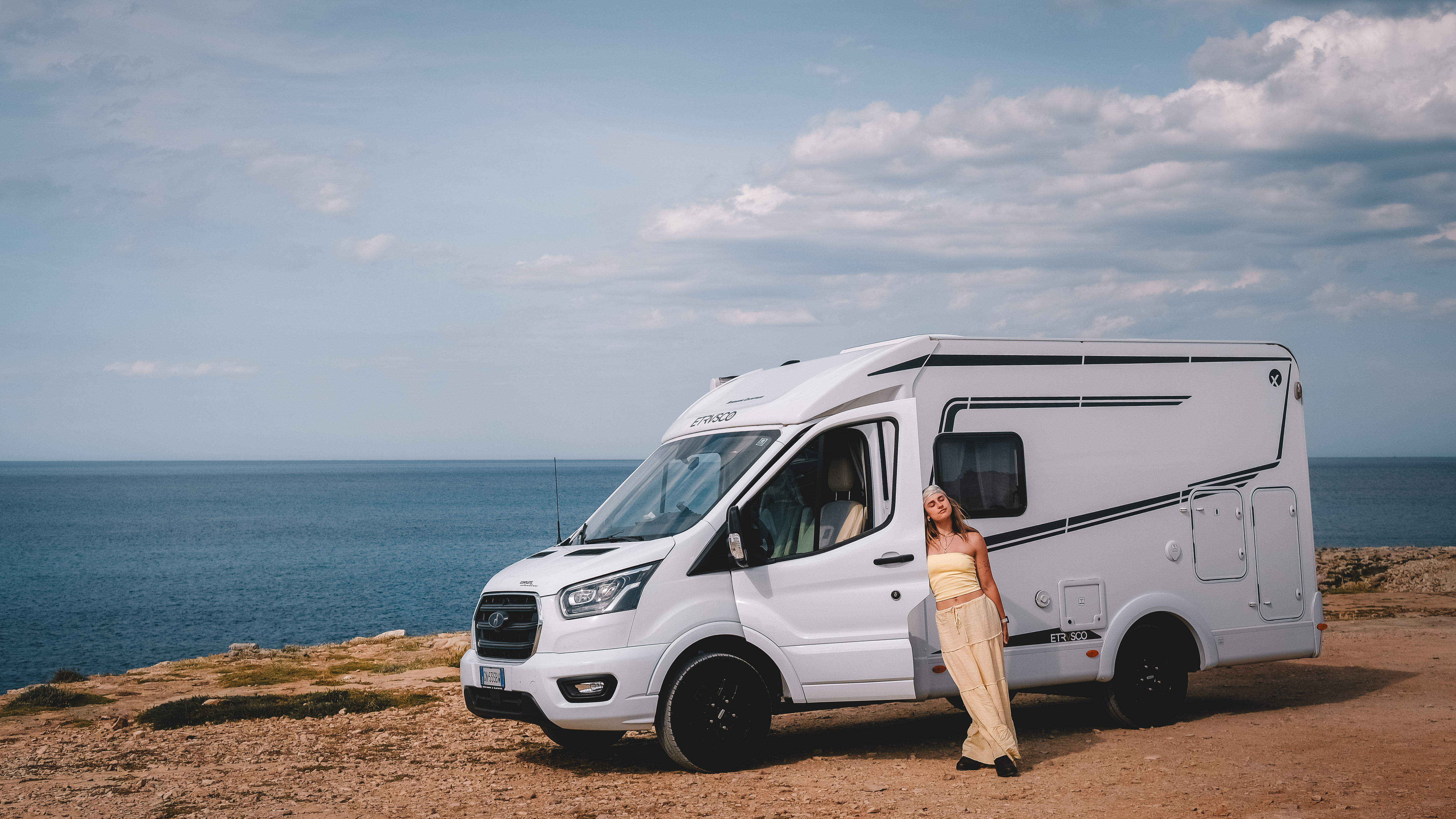 Frau lehnt sich gegen Wohnmobil am Meer