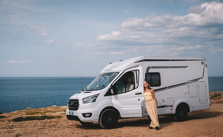 Frau lehnt sich gegen Wohnmobil am Meer
