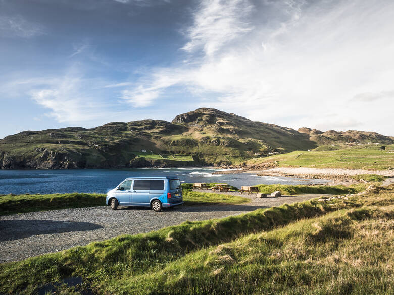 Blauer Campervan steht am Wasser in Irland 