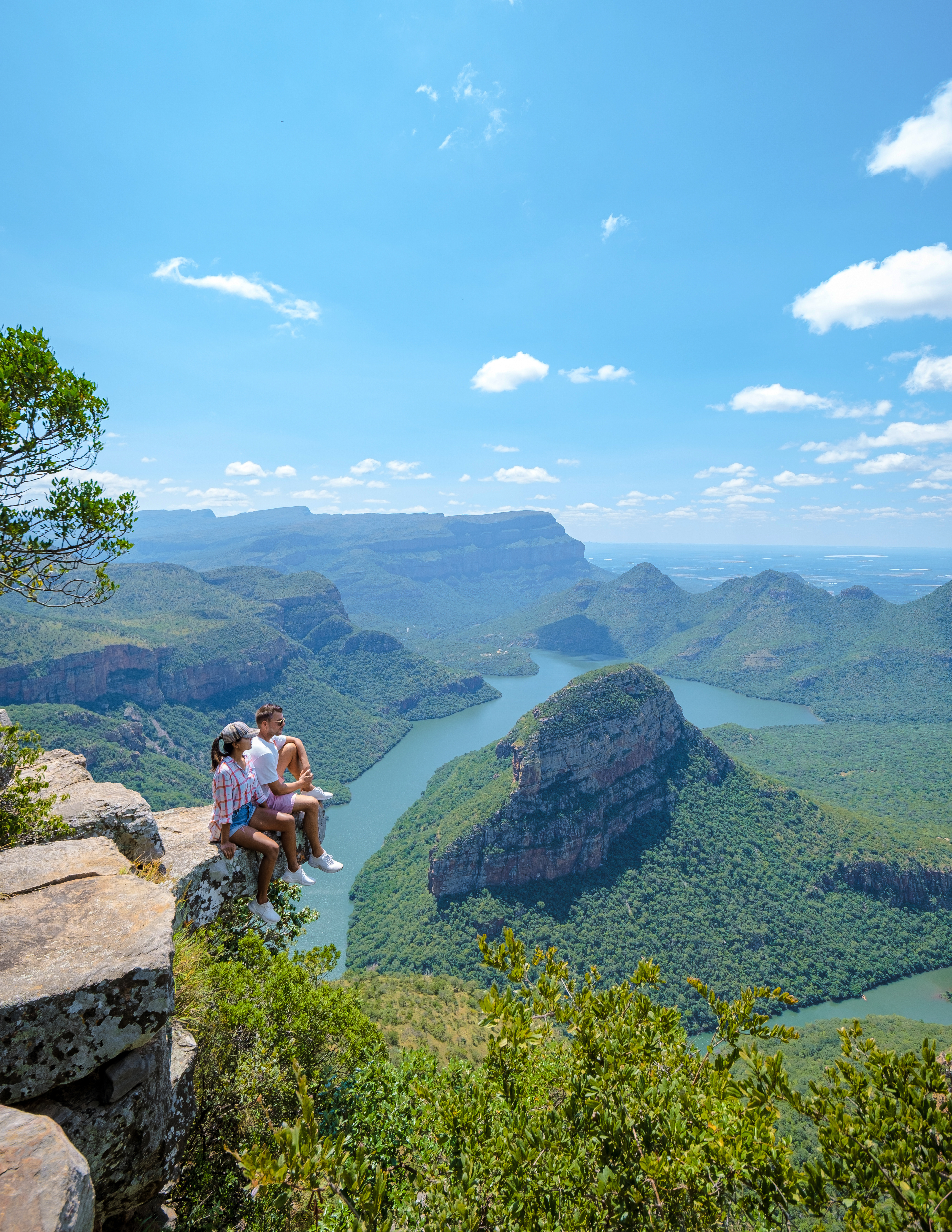 Zwei Personen sitzen auf einem Felsen und schauen auf die Three Rondavels in Südafrika