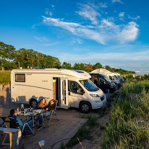 Wohnmobil in der Natur mit Campern, die vor ihrem Wohnmobil sitzen