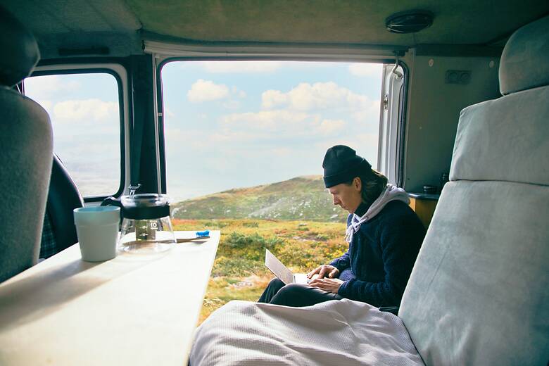 Mann sitzt mit einem Laptop im Camper vor einer Bergkulisse
