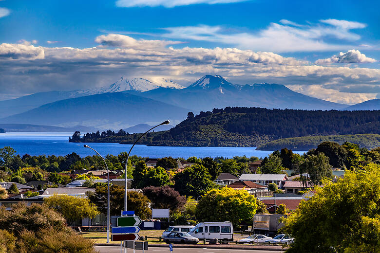 Wohnnmobile und Autos in einem urbanen Umfeld in Neuseeland, im Hintergrund die Berge und das Meer