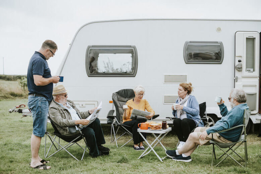 Camping para seniors: compañeros de camping pasan el rato juntos delante de una autocaravana.