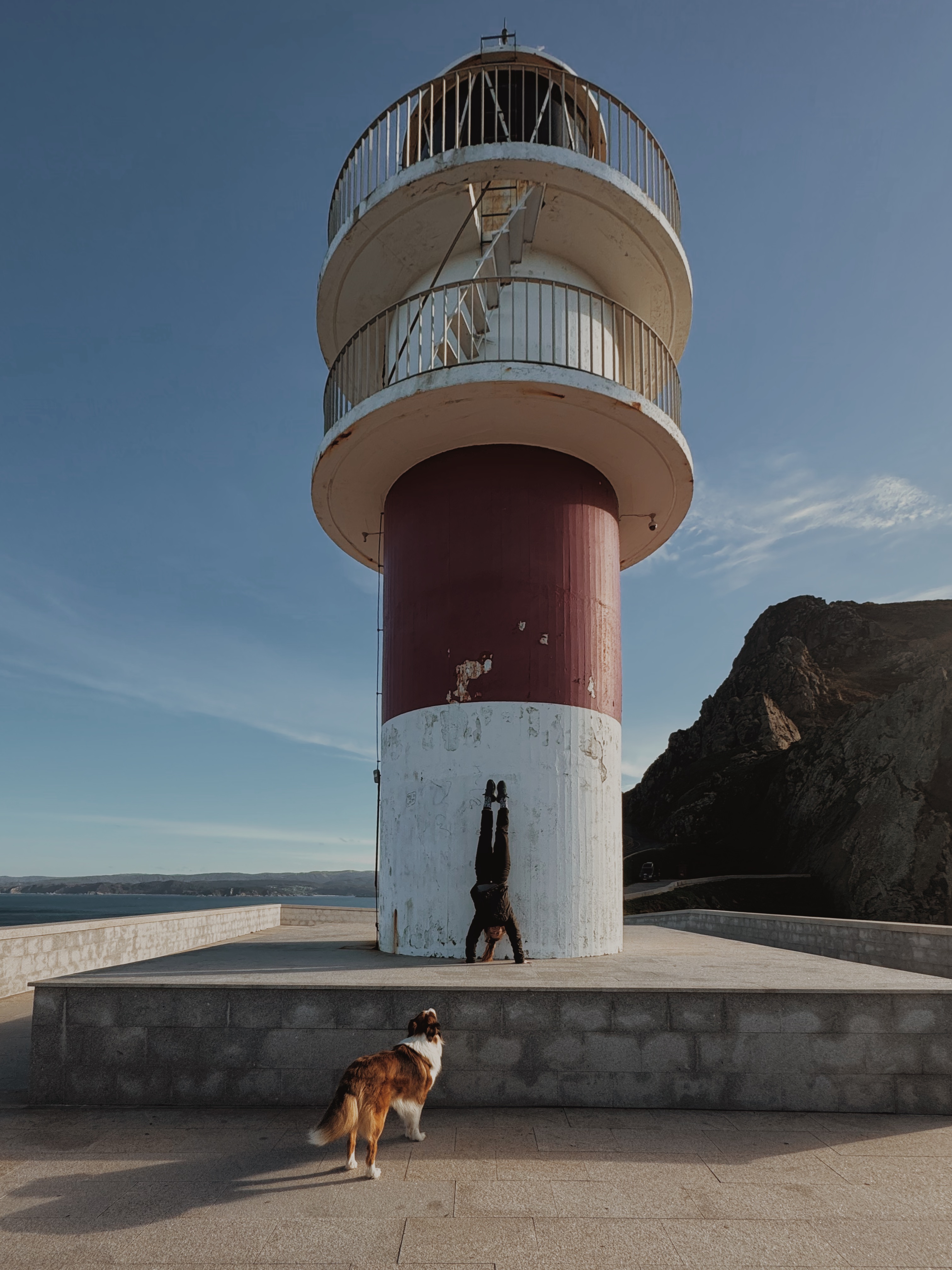 Frau macht einem Kopfstand an einem Leuchtturm in Spanien