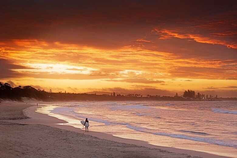 Frau mit Surfbrett bei Sonnenuntergang an einem australischen Strand