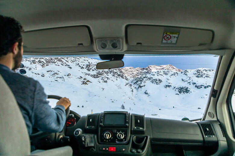 Mann sitzt im Wohnmobil und schaut durch die Frontscheibe auf eine Winterlandschaft