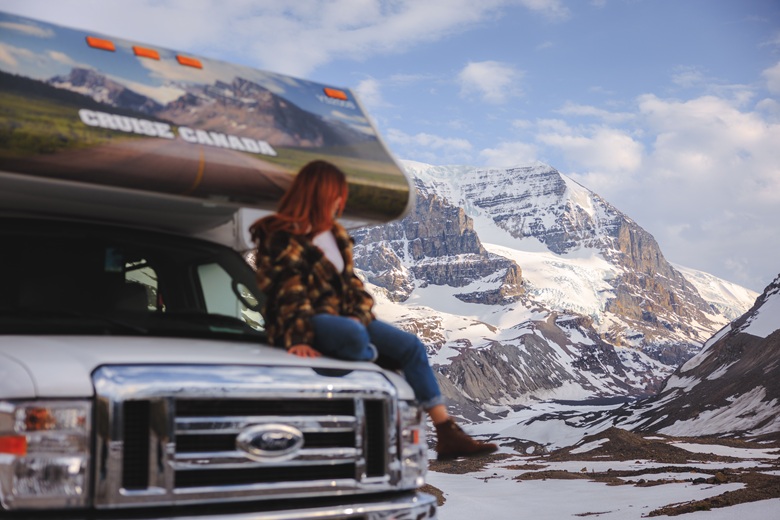 Frau sitzt auf einem Wohnmobil in einer verschneiten kanadischen Berglandschaft