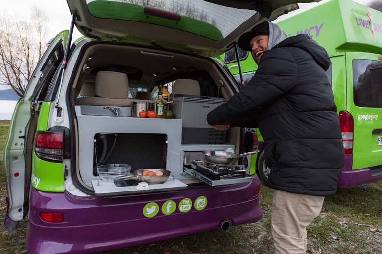 Mann mit Kapuzenpulli bereitet sich im JUCY Camper Essen zu