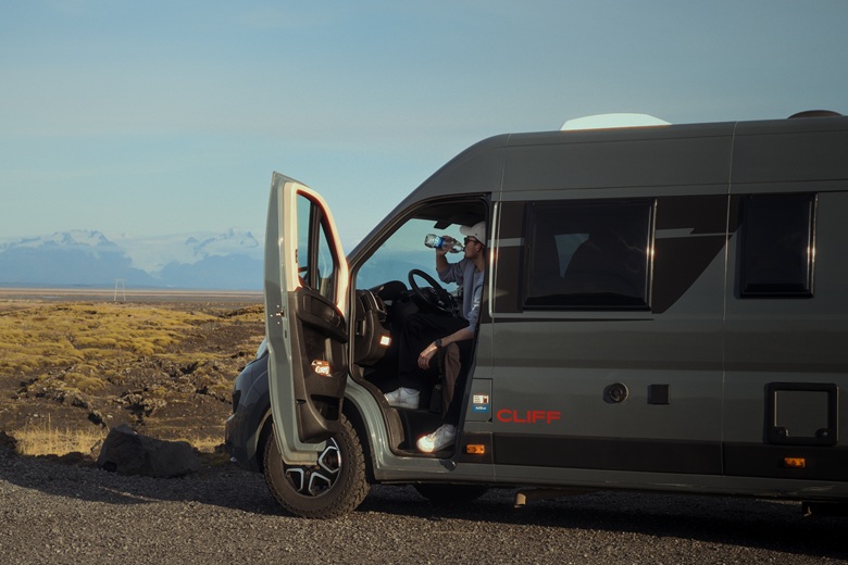 Mann sitzt im Campervan und trinkt aus einer Flasche Wasser