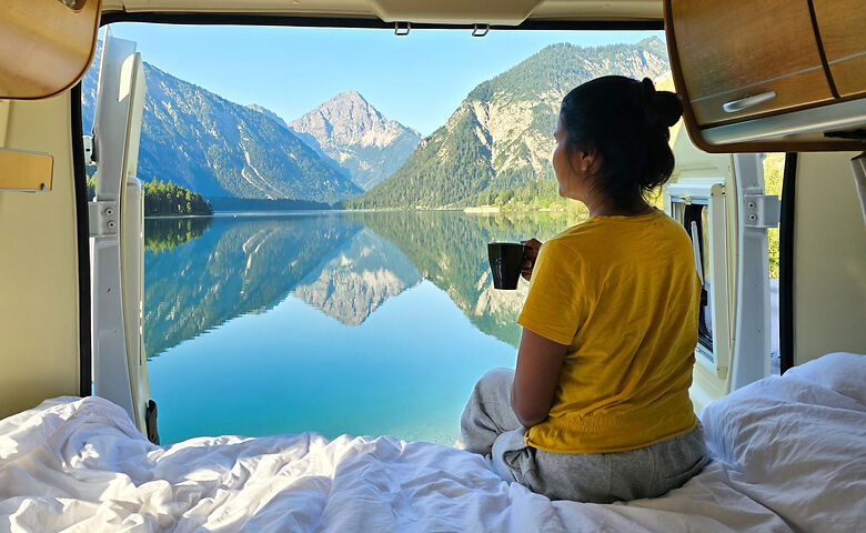 Frau trinkt einen Kaffee im Camper und schaut auf den Hallstätter See in Österreich