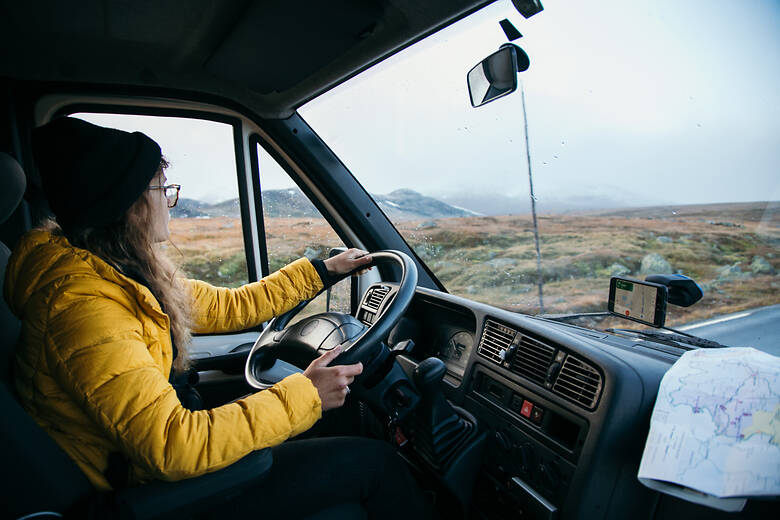 Frau sitzt hinter dem Steuer von einem Wohnmobil und fährt durch Island 