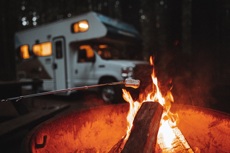 Marshmallow wird über dem Lagerfeuer gegrillt, im Hintergrund ein Wohnmobil