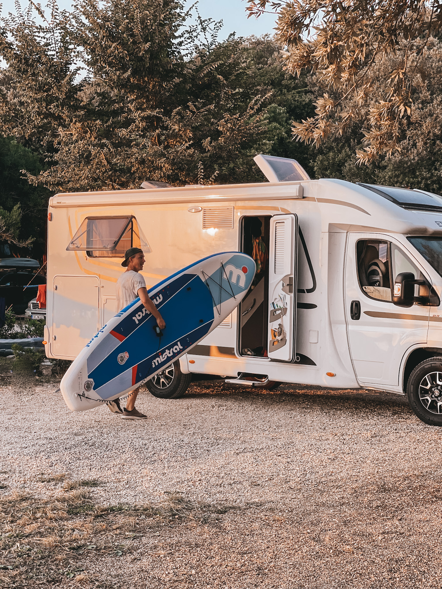 Mann mit Surfbrett vor dem Wohnmobil
