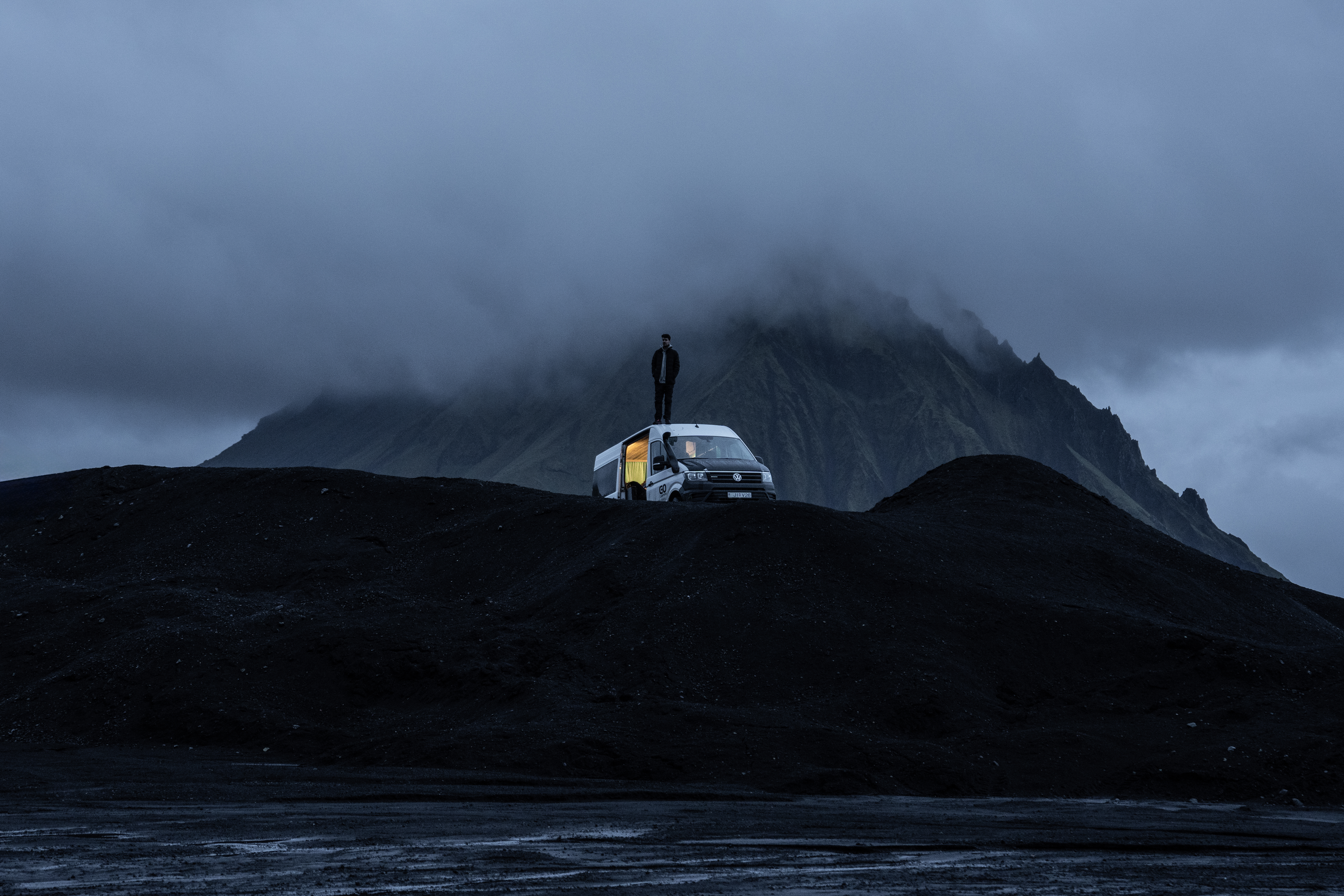 Mann auf einem Camper inmitten schwarzer Lavalandschaft in Island 