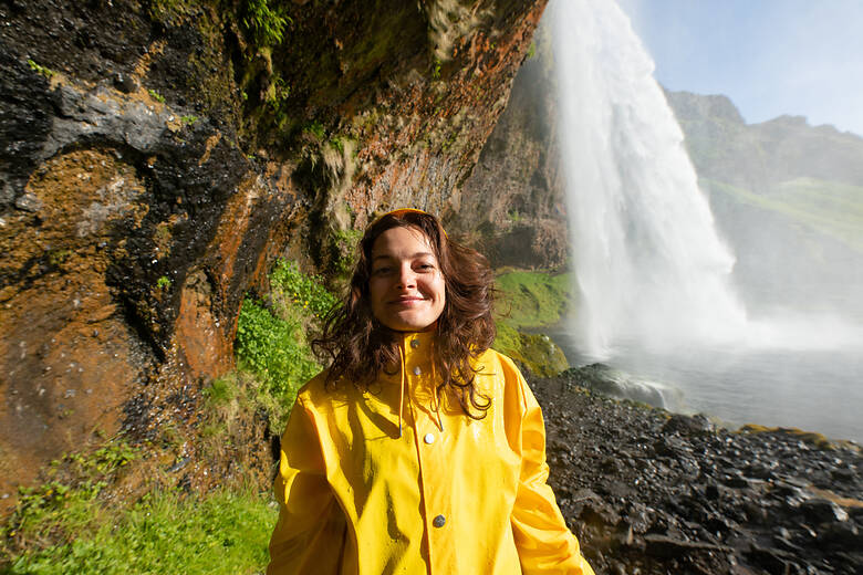 Frau an einem Wasserfall in Island in einer gelben Regenjacke 