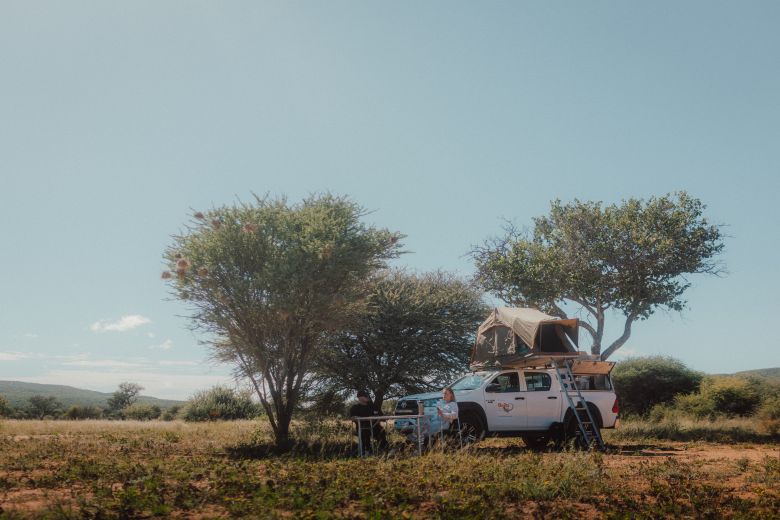 Zwei Personen sitzen vor einem Allrad-Camper mit Dachzelt in der Wildnis in Namibia 