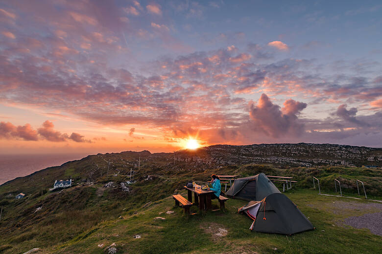 Frau sitzt bei Sonnenuntergang auf einem idyllischen Campingplatz in Irland