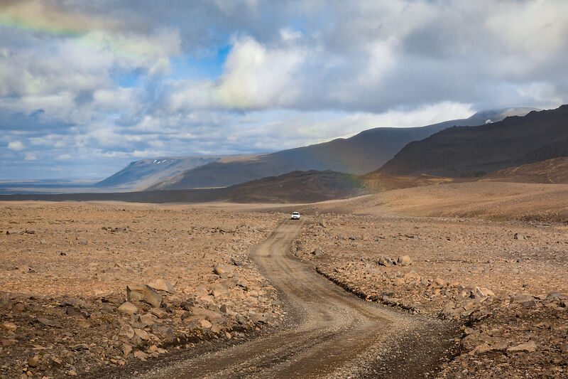 Auto fährt durch karge Landschaft in Islands Hochland 