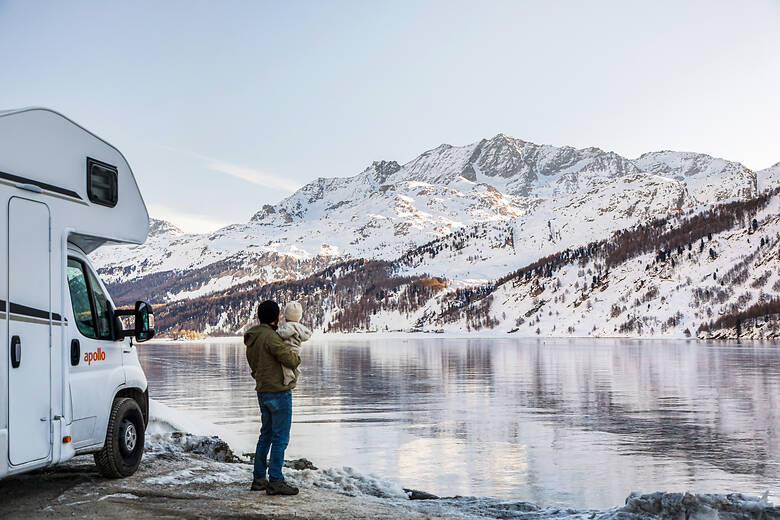 Mann mit Kind auf dem Arm in einer Winterlandschaft vor dem Wohnmobil