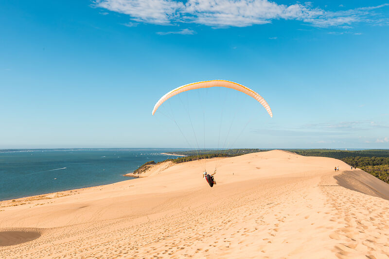 Ein Paraglider fliegt über die Dune du Pilat mit dem Meer im Hintergrund