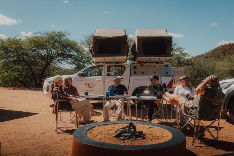 Freunde sitzen gemeinsam vor einem Allrad-Camper in Namibia und unterhalten sich 