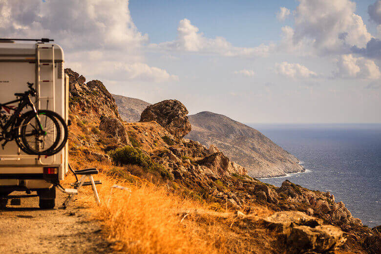 Campervan tour – an RV with mountain bikes at the back drives along the coast.