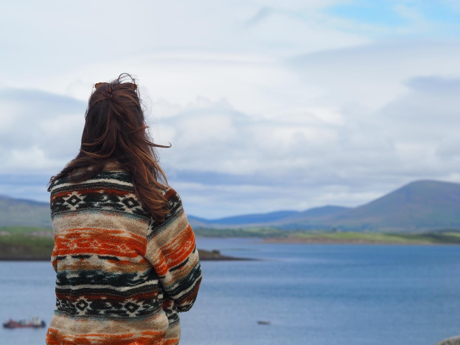 Een vrouw kijkt uit over de zee en de bergen in Ierland 