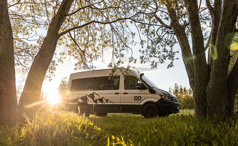 Camper parkt im Schatten unter Bäumen