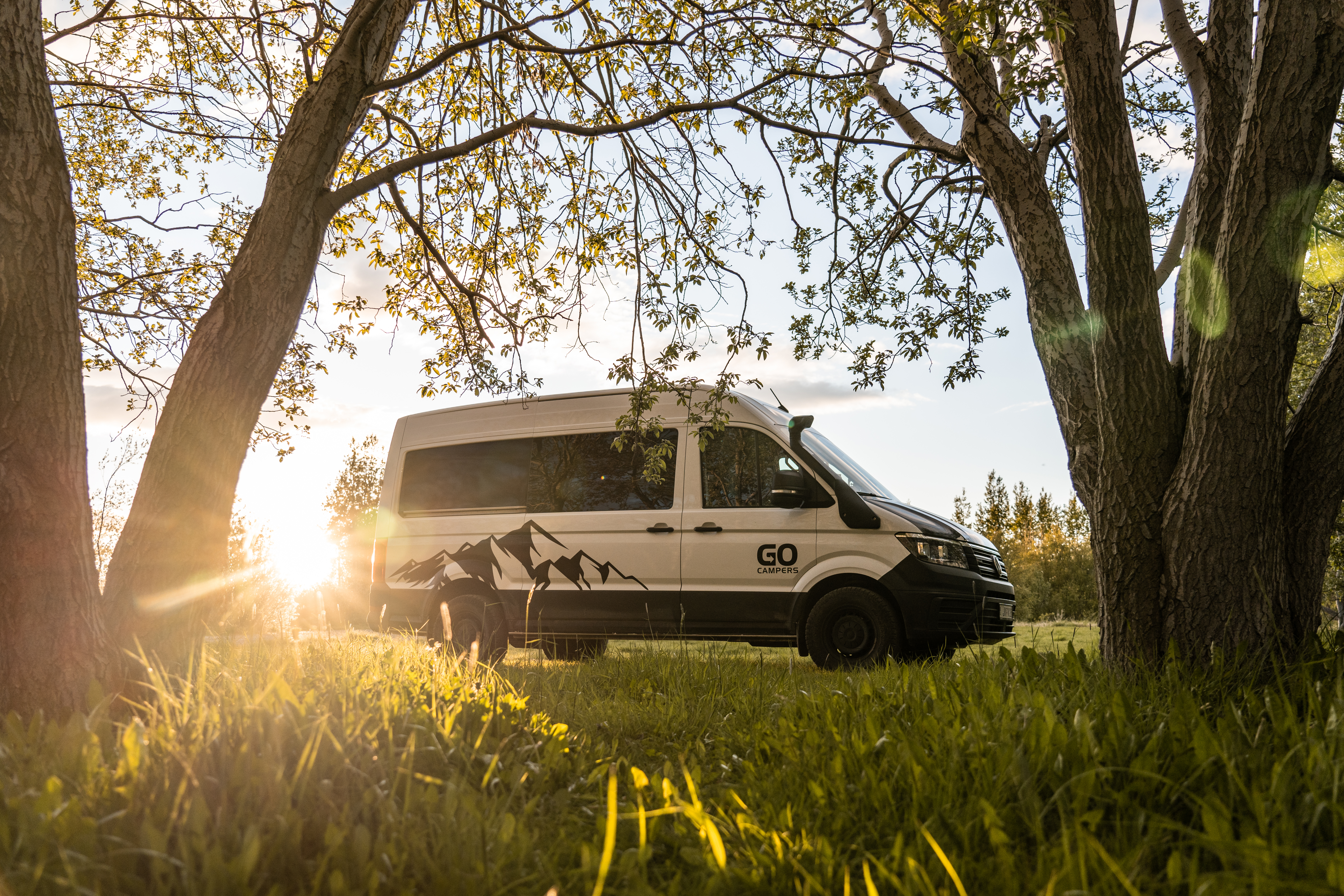 Camper parkt im Schatten unter Bäumen
