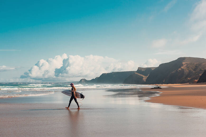 Frau mit einem Surfbrett unter dem Arm am Strand in Portugal