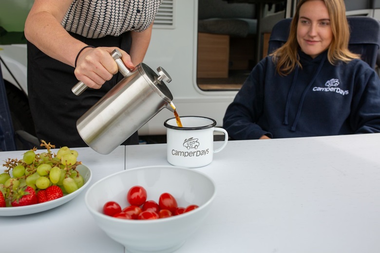 Frau schüttet Kaffee aus einer Thermoskanne in eine Camper-Tasse