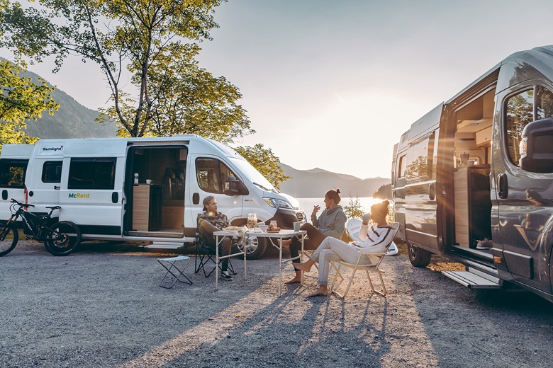 Freunde sitzen vor McRent-Campern und unterhalten sich