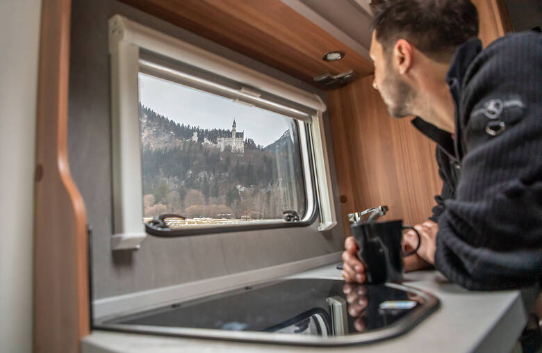 Mann schaut aus dem Wohnmobilfenster auf Schloss Neuschwanstein