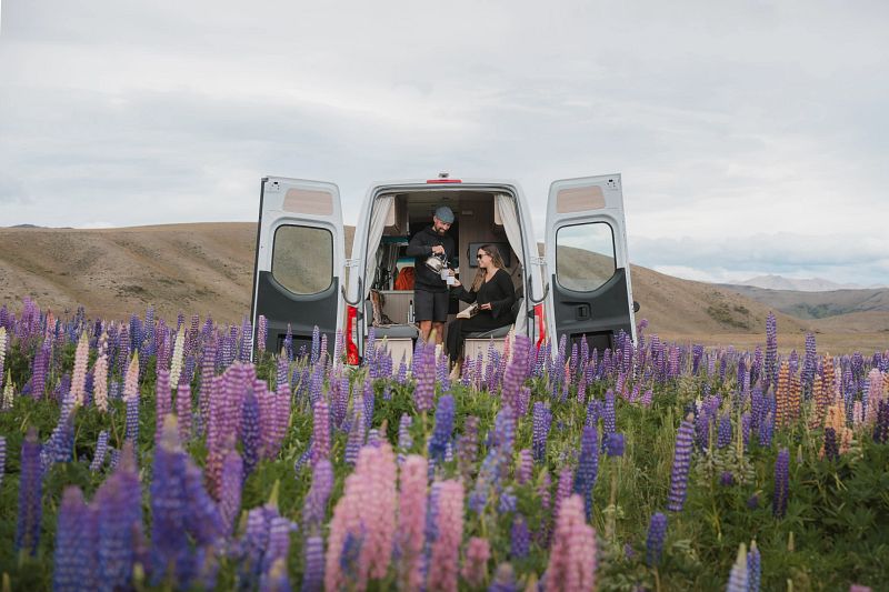 Paar sitzt in einem Camper auf einer bunten Blumenwiese
