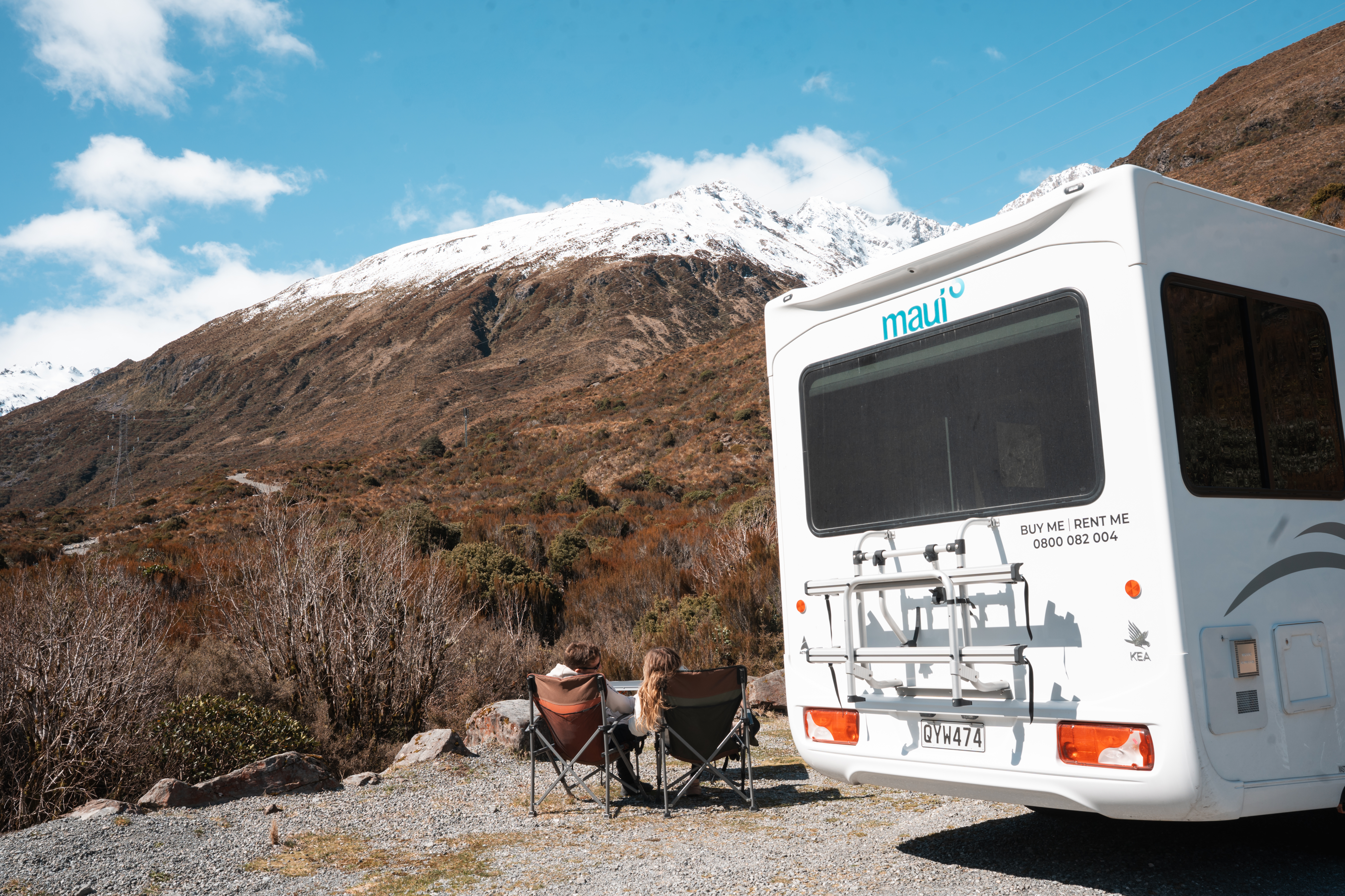  Paar in Camping-Stühlen neben dem Wohnmobil in Neuseeland 