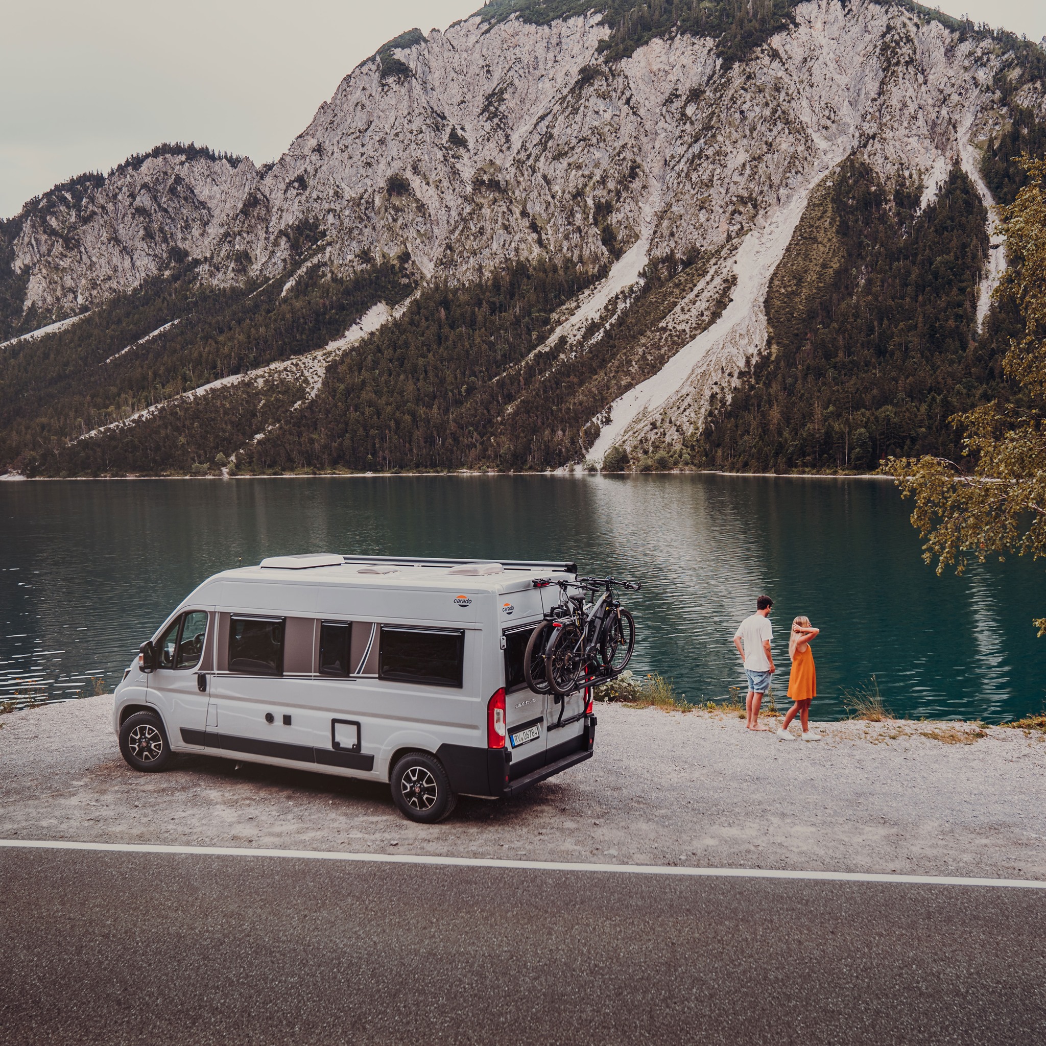 Paar steht mit einem Campervan an einem Bergsee