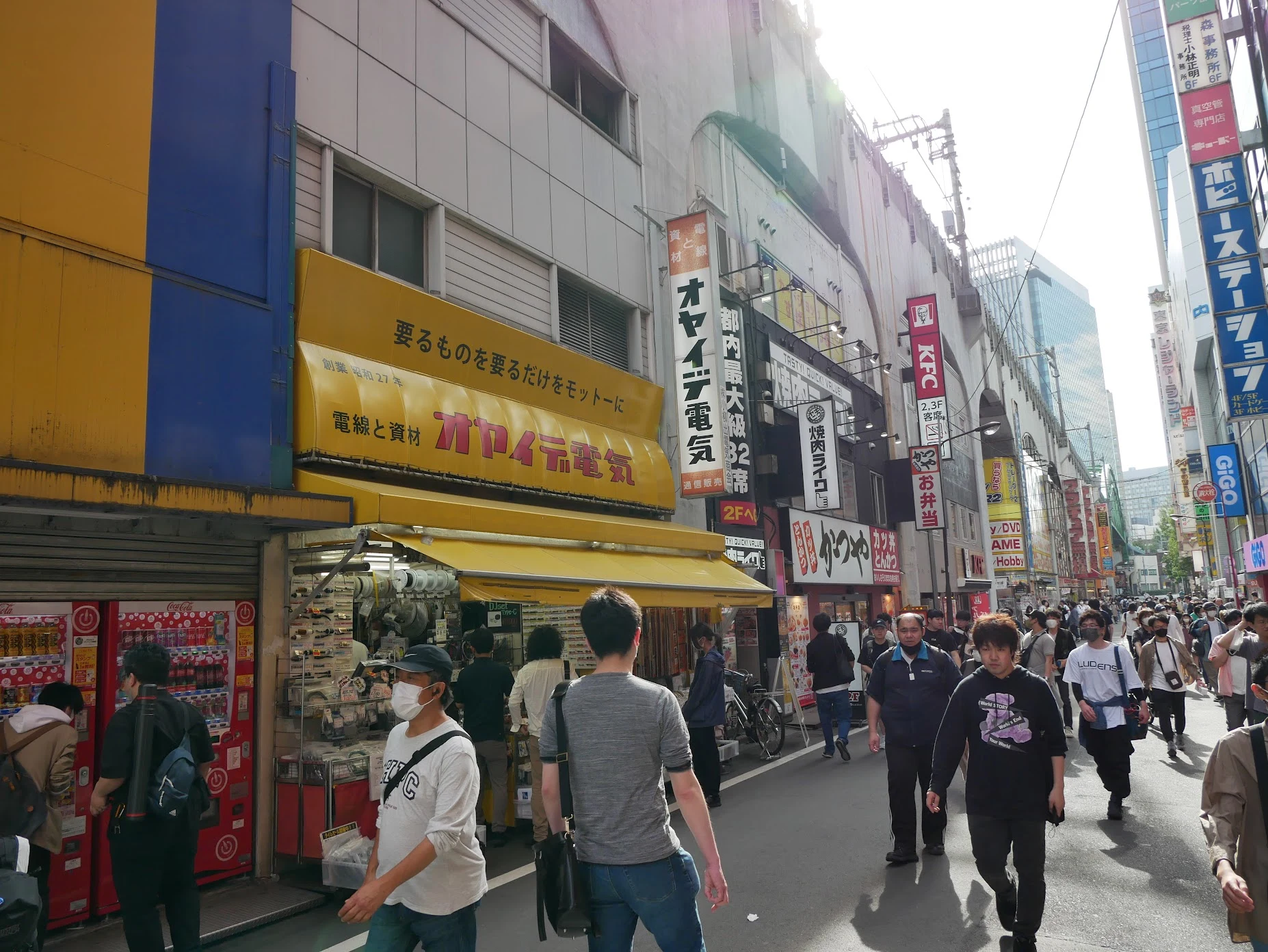 Akihabara street in Tokyo: yellow Oyaide Denki electronics shop awning on the left, dense vertical signage on the right.