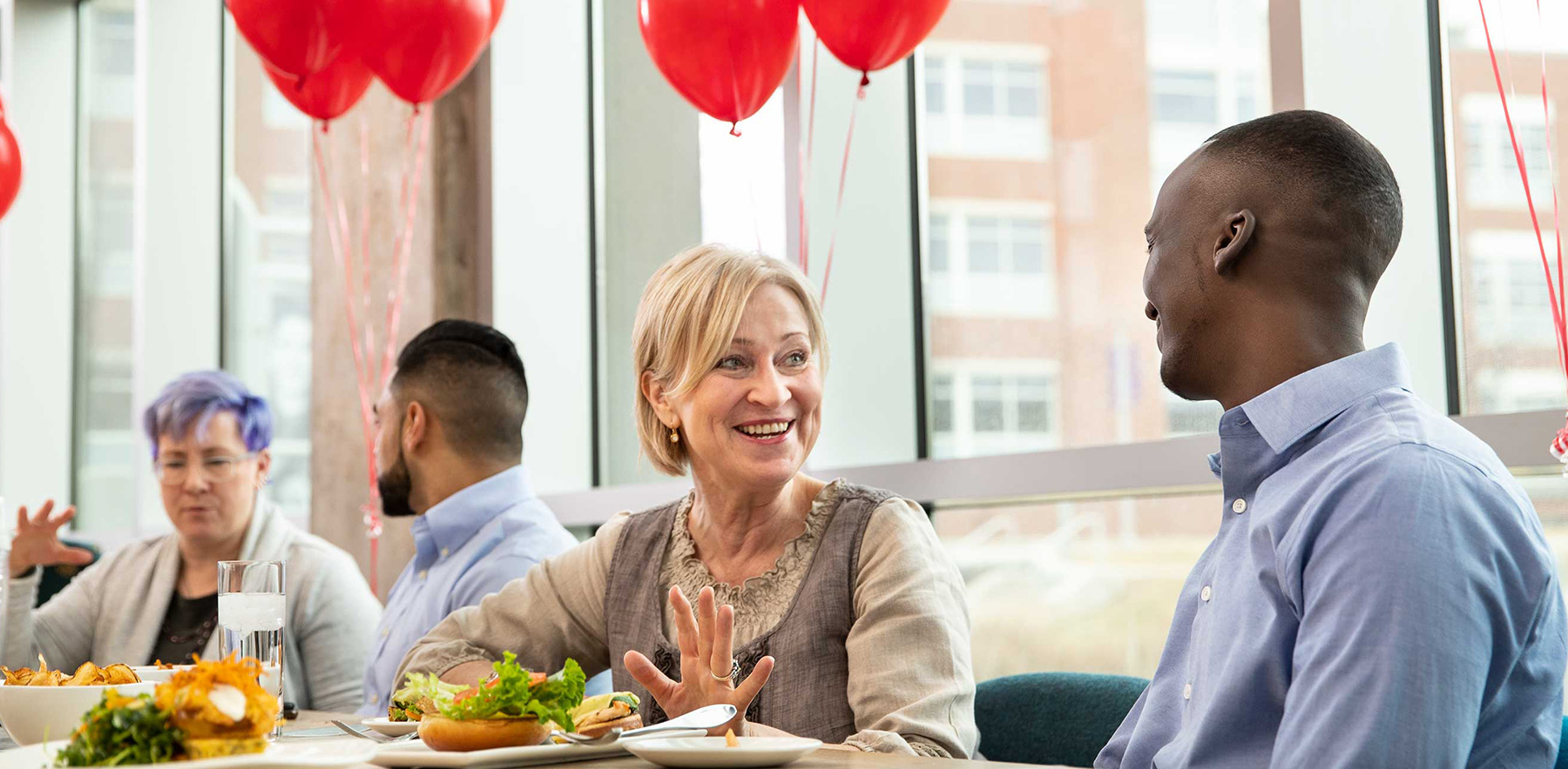 people talking at the table of a team building lunch with red balloons