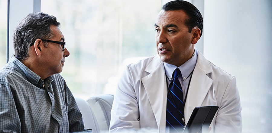 Multicultural doctor pointing to tablet and talking to male patient