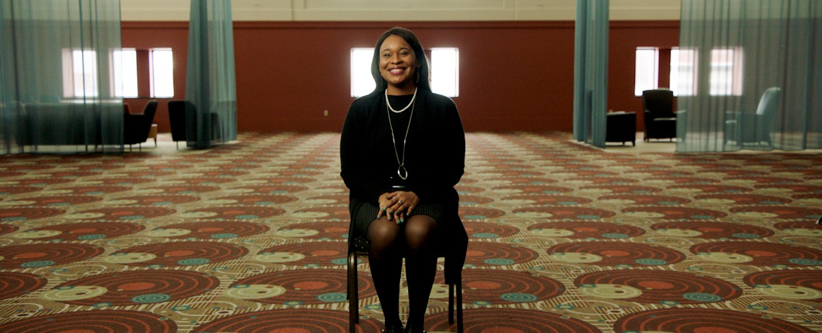 Dr. Christalyn Rhodes, seated in chair in large room and facing camera, smiling