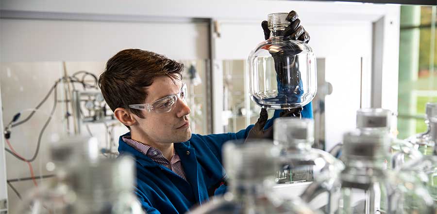 male scientist with goggles looking at glass jar