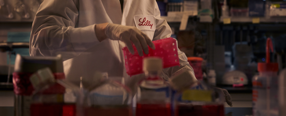 A person working in a lab facility wearing a white lab coat with a Lilly logo. 