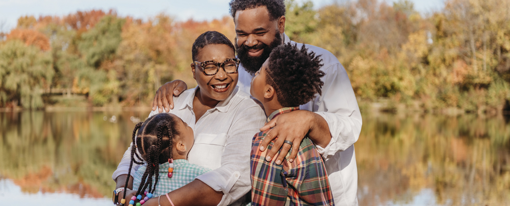 Lakia, her husband, and two kids hug and pose in front of a lake in the fall