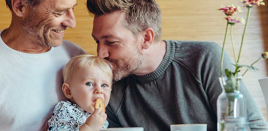 baby being kissed by dad at breakfast table