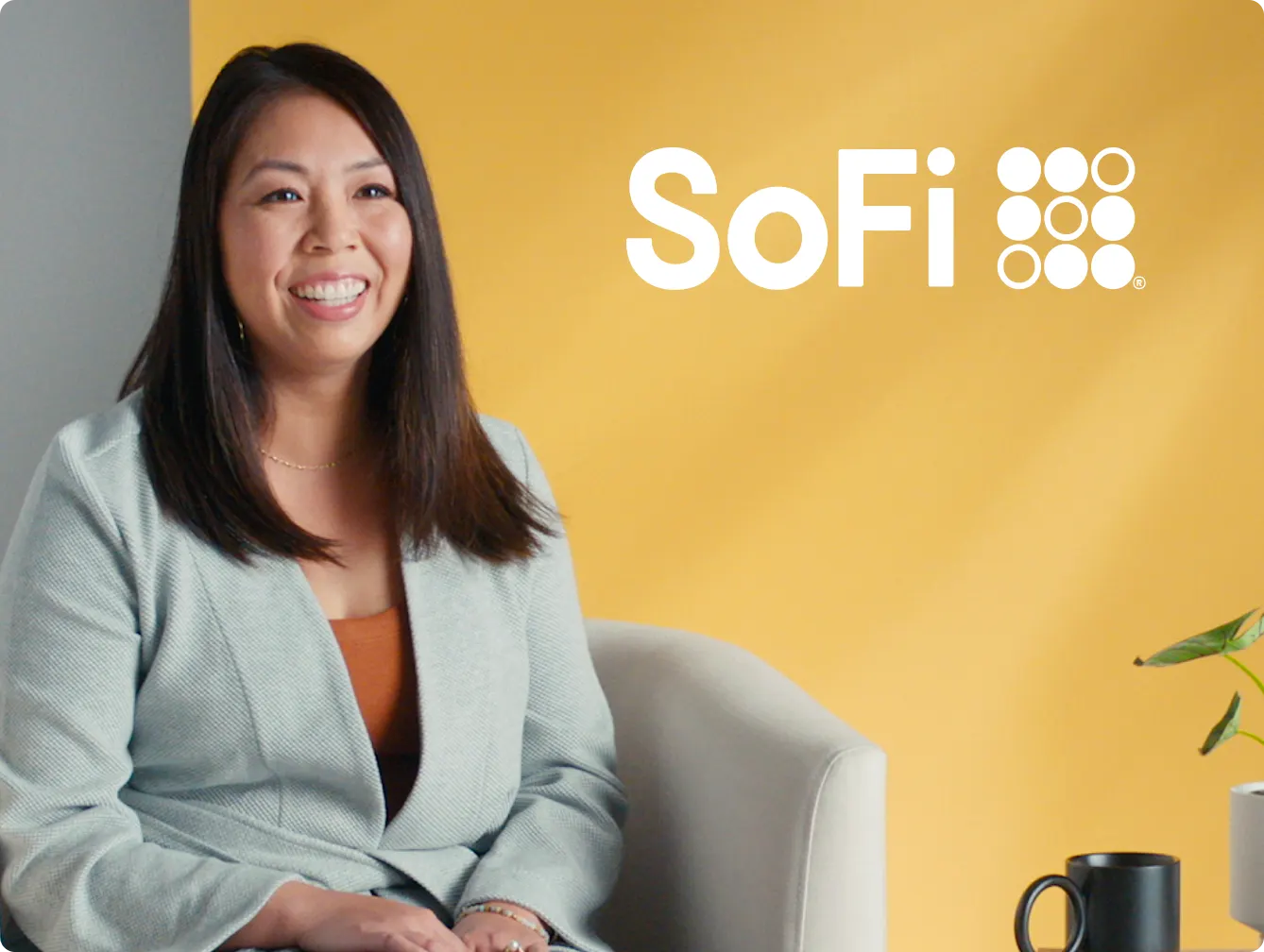 SoFi advertisement featuring a smiling woman with long dark hair, wearing a light gray blazer and an orange top, sitting on a chair. Next to her is a small table with a plant and a black mug. The SoFi logo is prominently displayed at the top right of the image on a yellow background.

