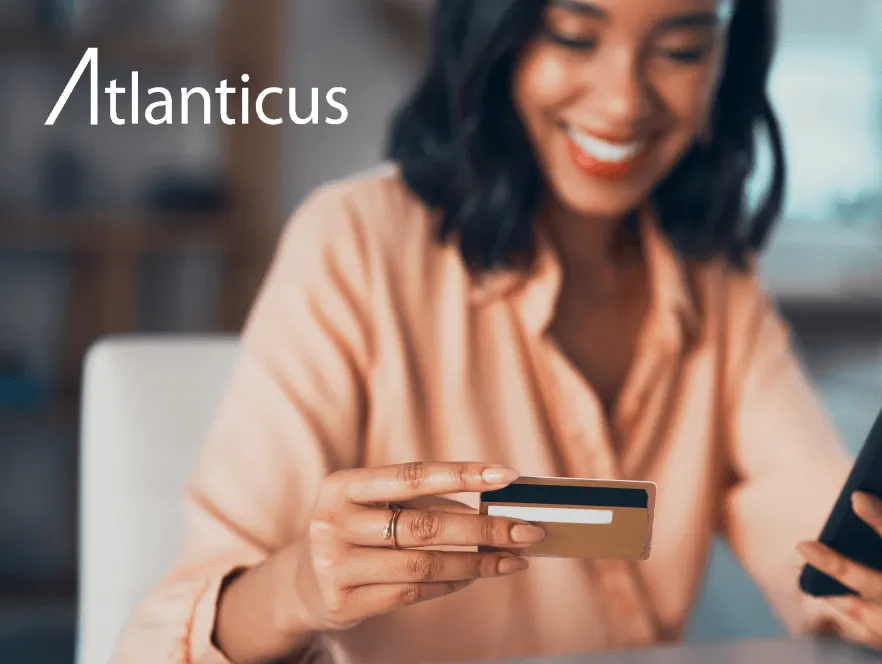 Atlanticus customer using a credit card and mobile phone to complete a digital payment, illustrating how Plaid's open banking APIs support secure consumer lending, account connectivity, and seamless financial experiences