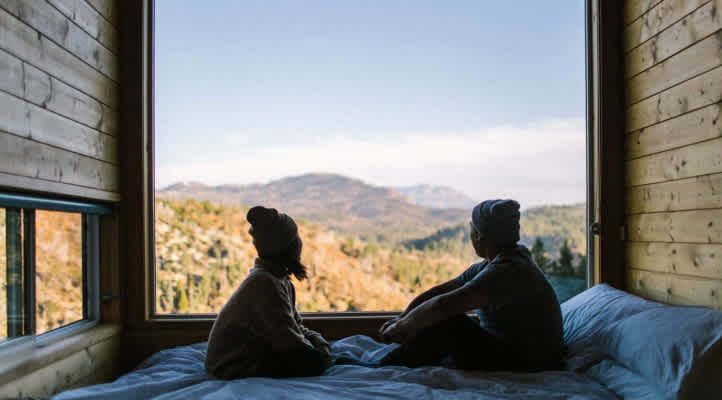 Photo of two people facing each other while looking out of the large window in a Getaway cabin.