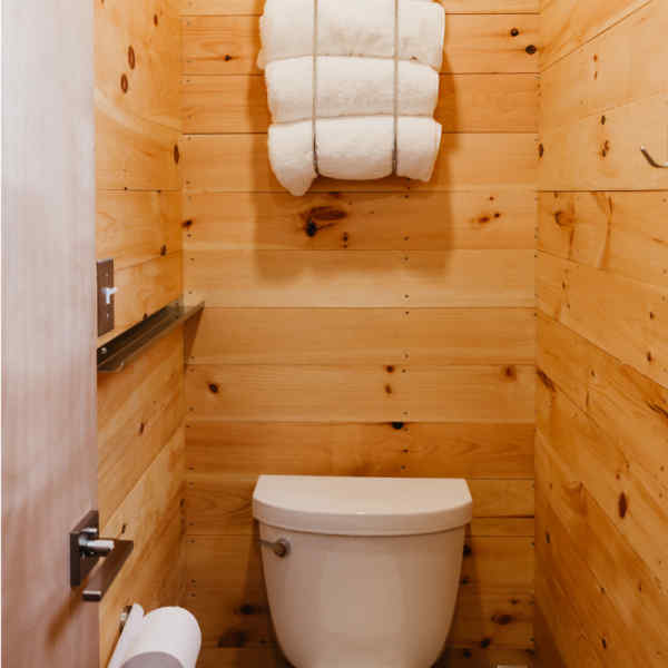Getaway cabin bathroom with flushing toilet, bath towels, lights, and toilet paper. 